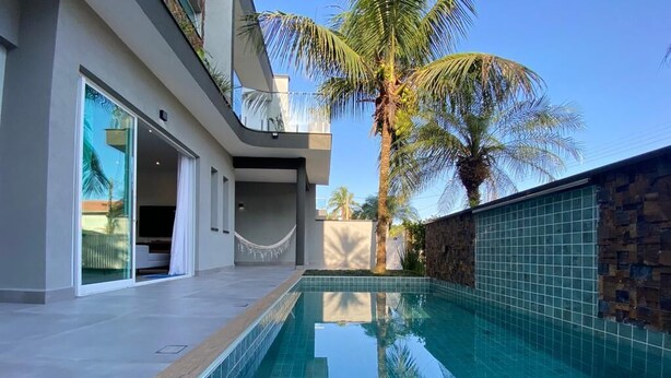 Un área de piscina moderna con una piscina cristalina, un muro de piedra y una palmera.