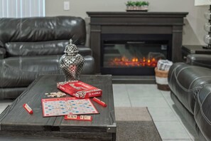 Ein Wohnzimmer mit Kamin, einem Couchtisch mit Scrabble-Kacheln, einer Scrabble-Box und einer dekorativen Vase.