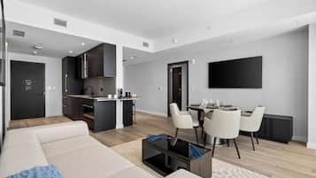 A modern apartment with a living area, dining space, kitchenette, and a flat-screen TV mounted on the wall.