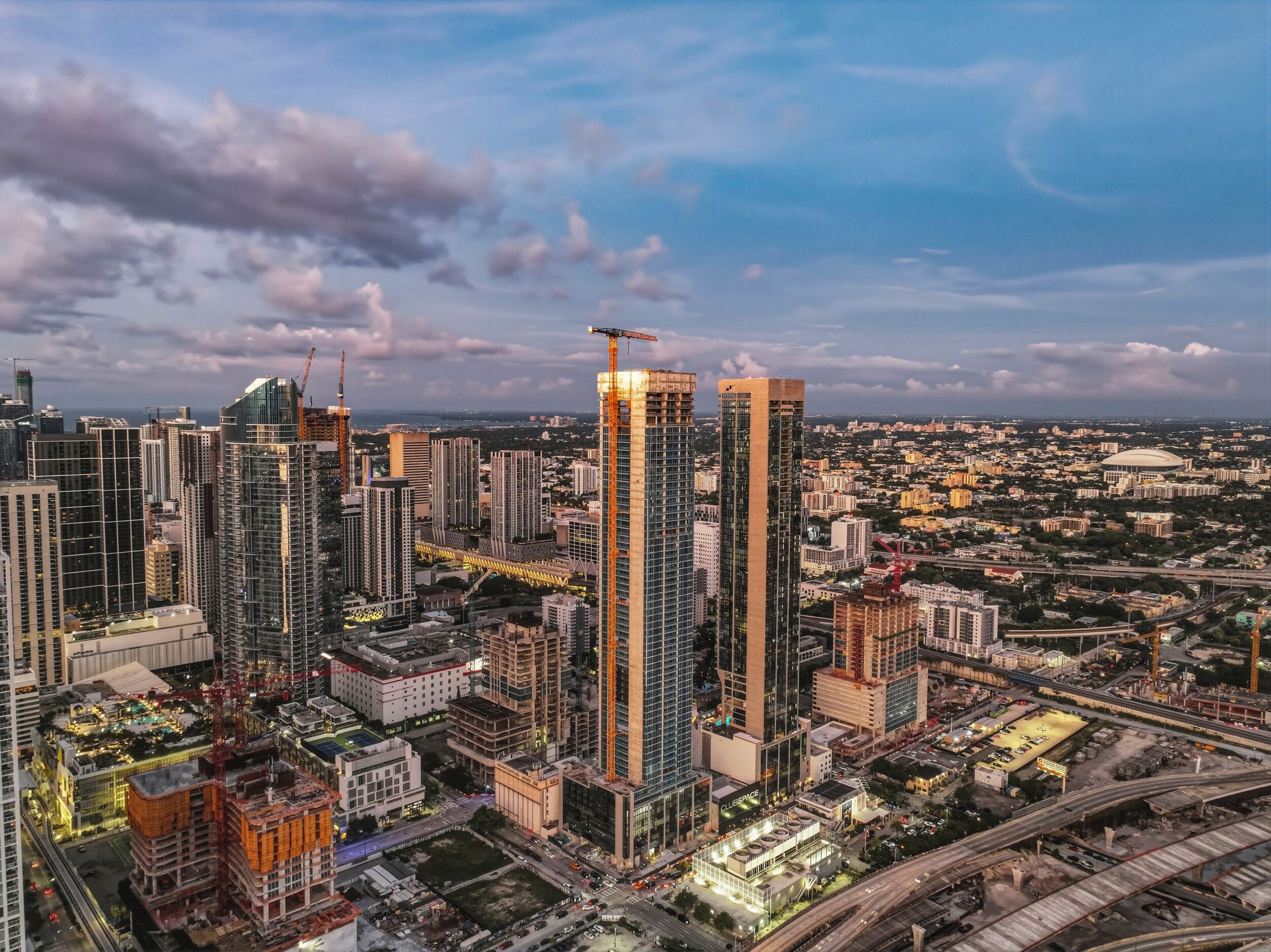 A cityscape with high-rise buildings, construction cranes, and a large stadium.