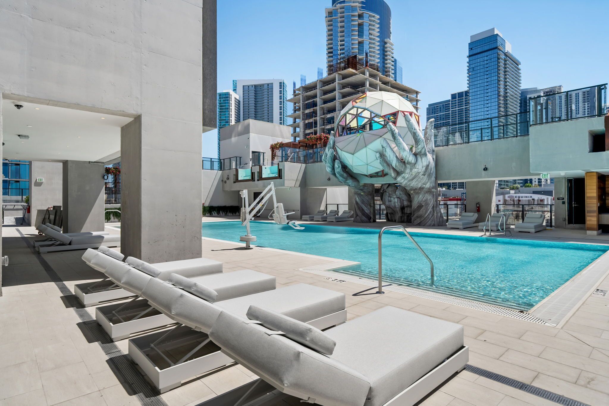 A rooftop pool with lounge chairs, a unique sculpture, and a city skyline in the background.