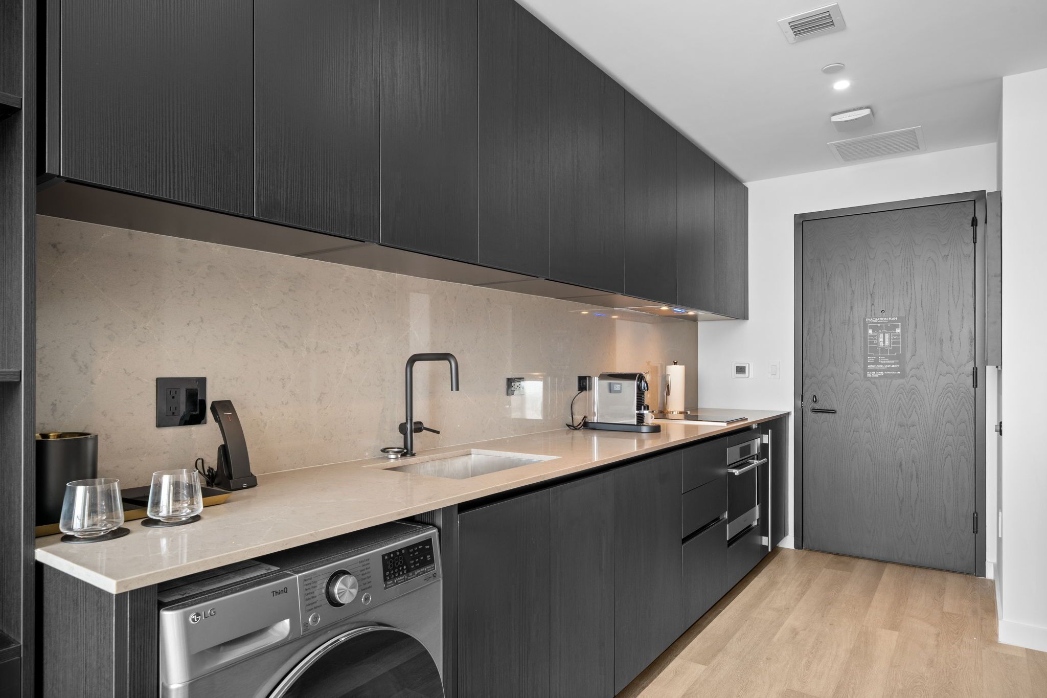 A modern kitchen with dark cabinetry, a built-in dishwasher, a sink, and a countertop.