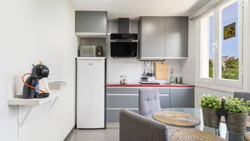 Une cuisine compacte dotée d’appareils électroménagers modernes, un coin repas avec une table et des chaises en verre, et une vue par la fenêtre.