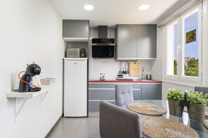A compact kitchen with modern appliances, a dining area with a glass table and chairs, and a view through a window.