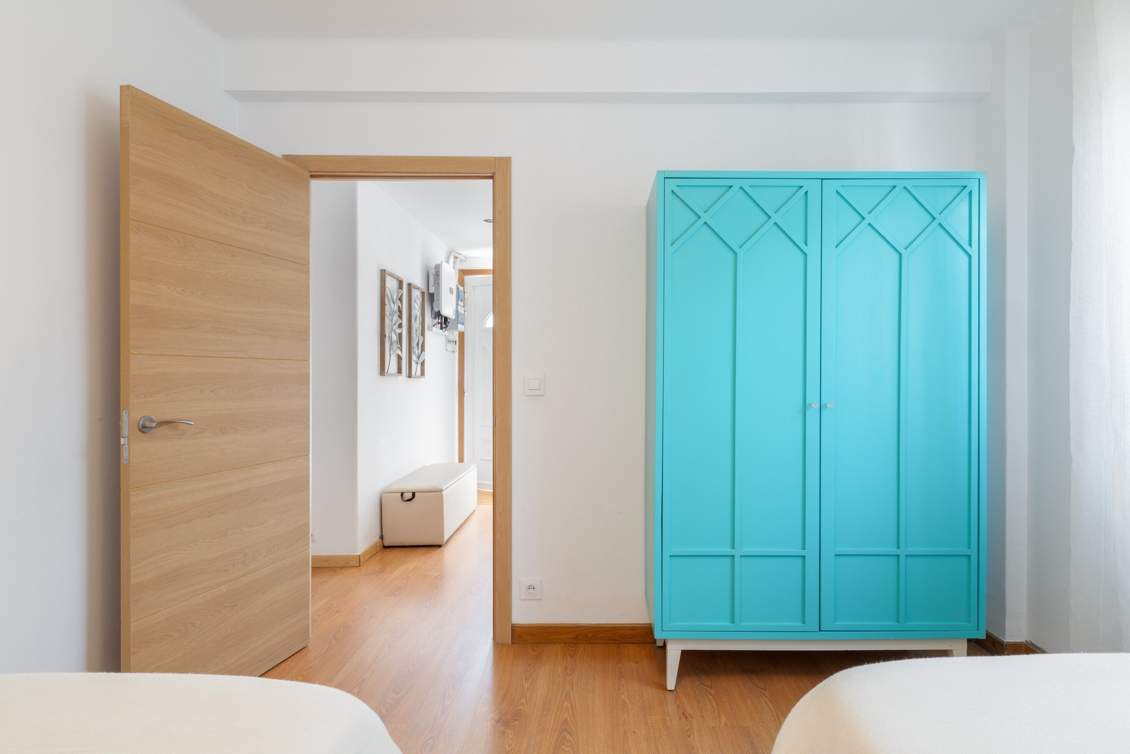 Ein Schlafzimmer mit Holzschrank, weißem Bett und einem Flur, der in einen weiteren Raum führt.