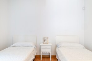 A twin room with two single beds, a small bedside table with a lamp, and a plain white wall.