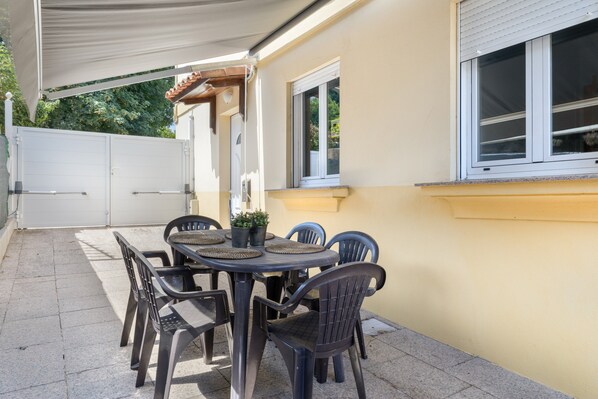 An outdoor patio with a round table and chairs, a covered area, and a white gate.