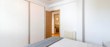 Un dormitorio con cama, armario, radiador y una puerta que da a otra habitación.