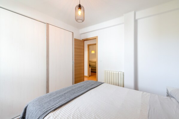 A bedroom with a bed, a wardrobe, a radiator, and a door leading to another room.
