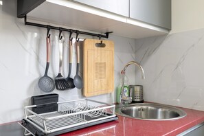A kitchen with a stainless steel sink, a dish rack, and various utensils hanging on the wall.