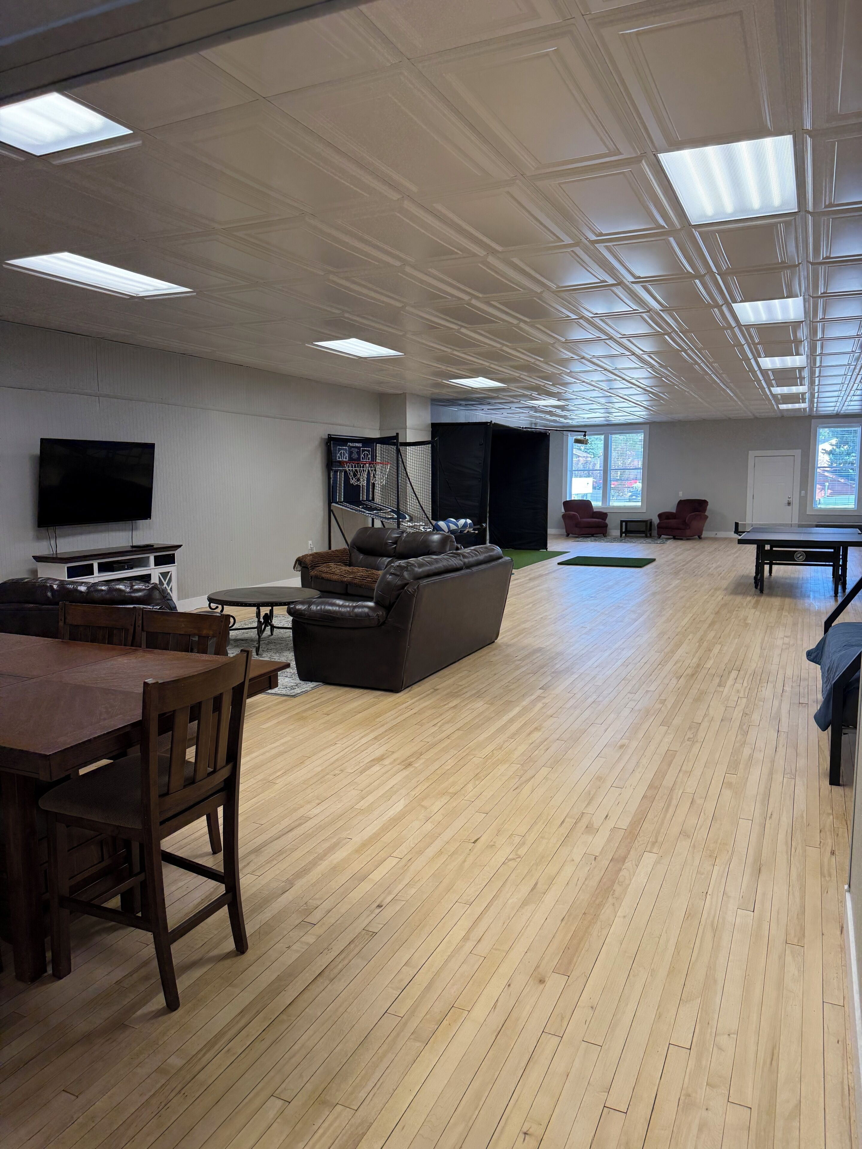A spacious room with a wooden floor, a large flat-screen TV, a basketball hoop, and a ping pong table.