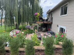 Ein Wohnhaus mit Terrasse, Sitzgelegenheit im Freien und einem Garten mit verschiedenen Pflanzen und Blumen.