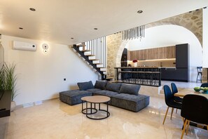 Ein moderner Wohnraum mit Ecksofa, einem kleinen runden Tisch und einer Treppe zu einer Küchenzeile.