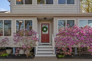 A two-story house with a front door, a wreath, and pink flowering bushes.