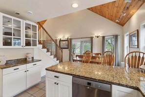 A kitchen with white cabinets, a granite countertop, a Bosch dishwasher, and a wooden staircase.