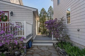Ein Wohnhaus mit einem Kiesweg, einer Veranda mit Gartenmöbeln und einem Garten mit blühenden Pflanzen.