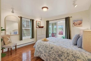Ein Schlafzimmer mit einem Bett, einem Sessel, einem Fenster mit Vorhängen, einer Deckenleuchte und einem Bild an der Wand.