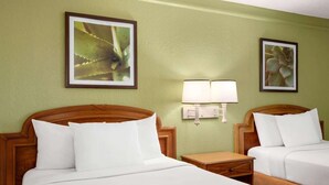 Habitación de hotel con dos camas, una mesita de noche, una lámpara de pared y dos láminas botánicas enmarcadas.
