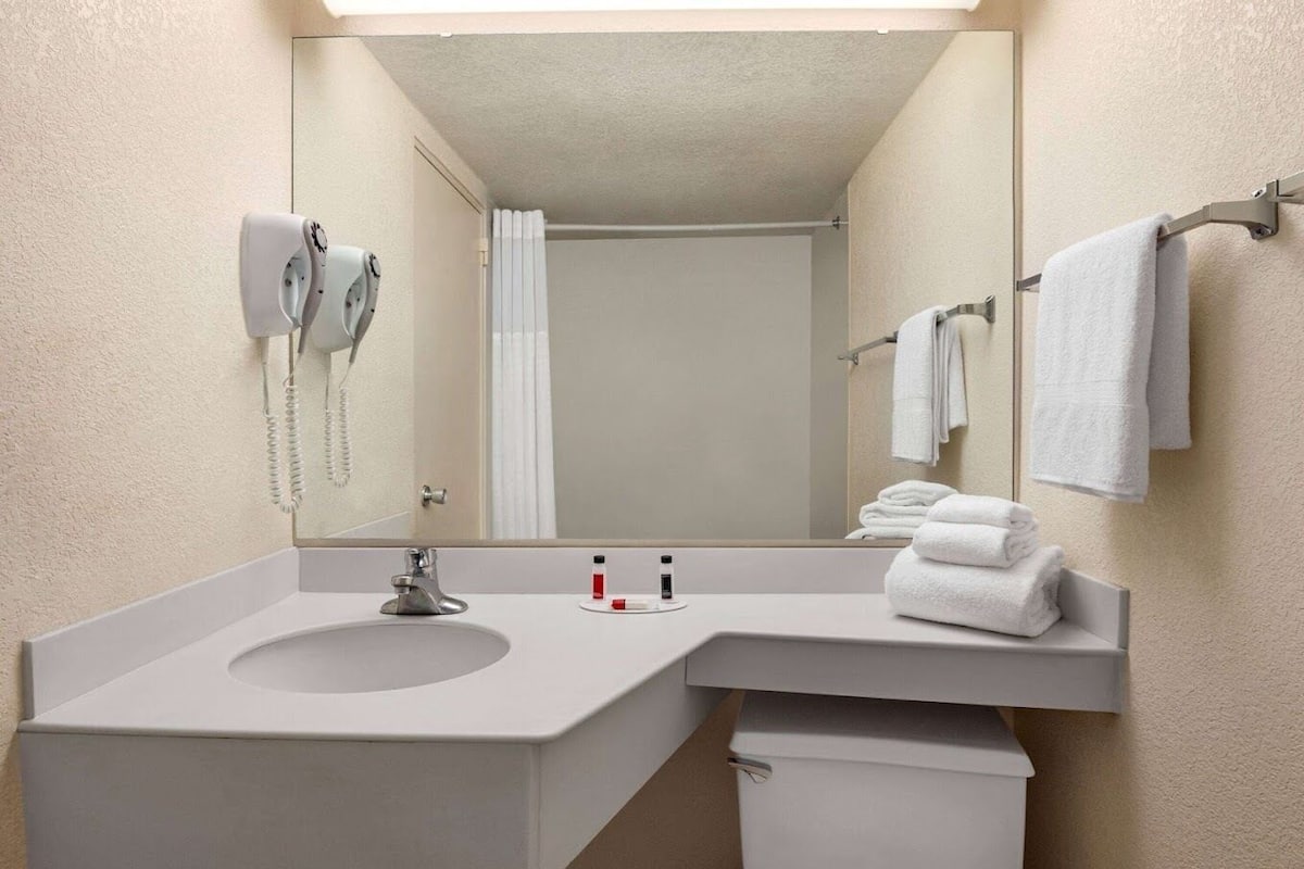 Un baño de hotel con un espejo grande, un lavamanos, un inodoro, un perchero para toallas y un secador de pelo.