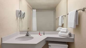 Un baño de hotel con un espejo grande, un lavamanos, un inodoro, un perchero para toallas y un secador de pelo.