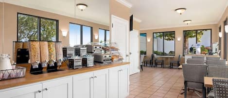 A breakfast bar with cereal dispensers, a coffee machine, and a fruit display. There are chairs and tables in the dining area.
