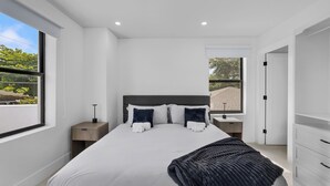 Een moderne slaapkamer met een groot bed, nachtkastjes, een garderobe en uitzicht op de omgeving.
