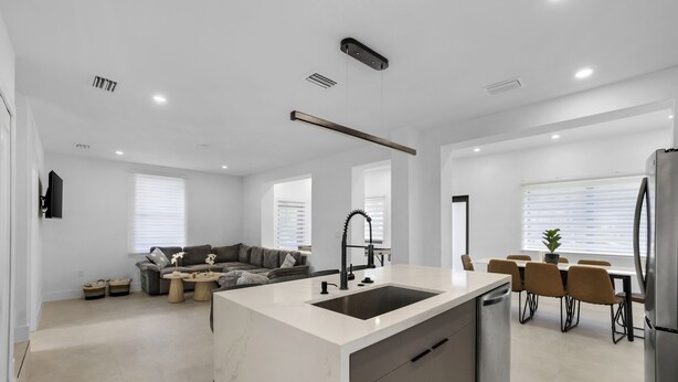 Een moderne keuken met een centraal kookeiland, een eethoek met stoelen, een bank en een koelkast.