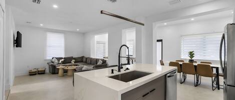 Una cocina moderna con una isla central, un comedor con sillas, un sofá y un refrigerador.