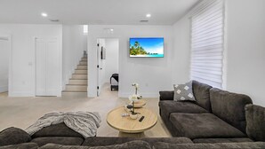 Een moderne woonkamer met een bank, een salontafel, een televisie en een trap naar een andere kamer.