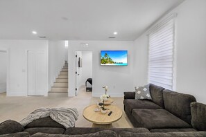 A modern living room with a sofa, a coffee table, a TV, and a staircase leading to another room. - Luxury Miami Villa w/ Pool, Jacuzzi, BBQ & Pickleball Court (Miami)