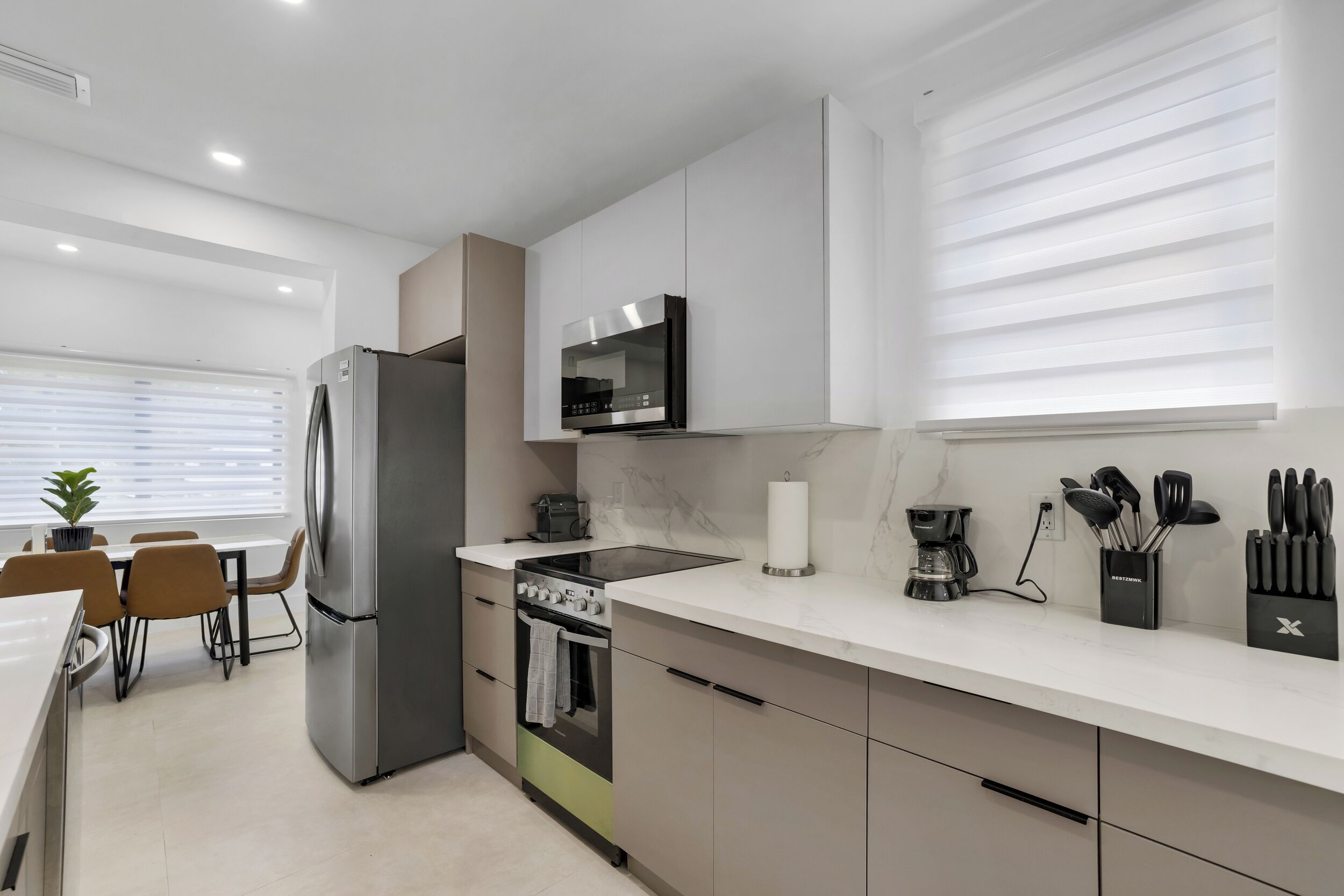 Eine moderne Küche mit Kühlschrank, Herd, Backofen und Mikrowelle. Ein Essbereich mit Stühlen und Tisch ist ebenfalls vorhanden.