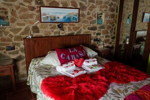 Un dormitorio con paredes de piedra, una cama, una mesita de noche, un espejo y un cuadro en la pared.