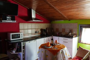 A compact kitchen with a microwave, stove, and dining area with a table set for two. - La Cabaña del Llano — private pool and garden on an Extremaduran estate, near Portugal (La Aceña de la Borrega)