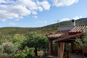Una casa con techo de tejas, chimenea de piedra y un pequeño balcón con macetas.