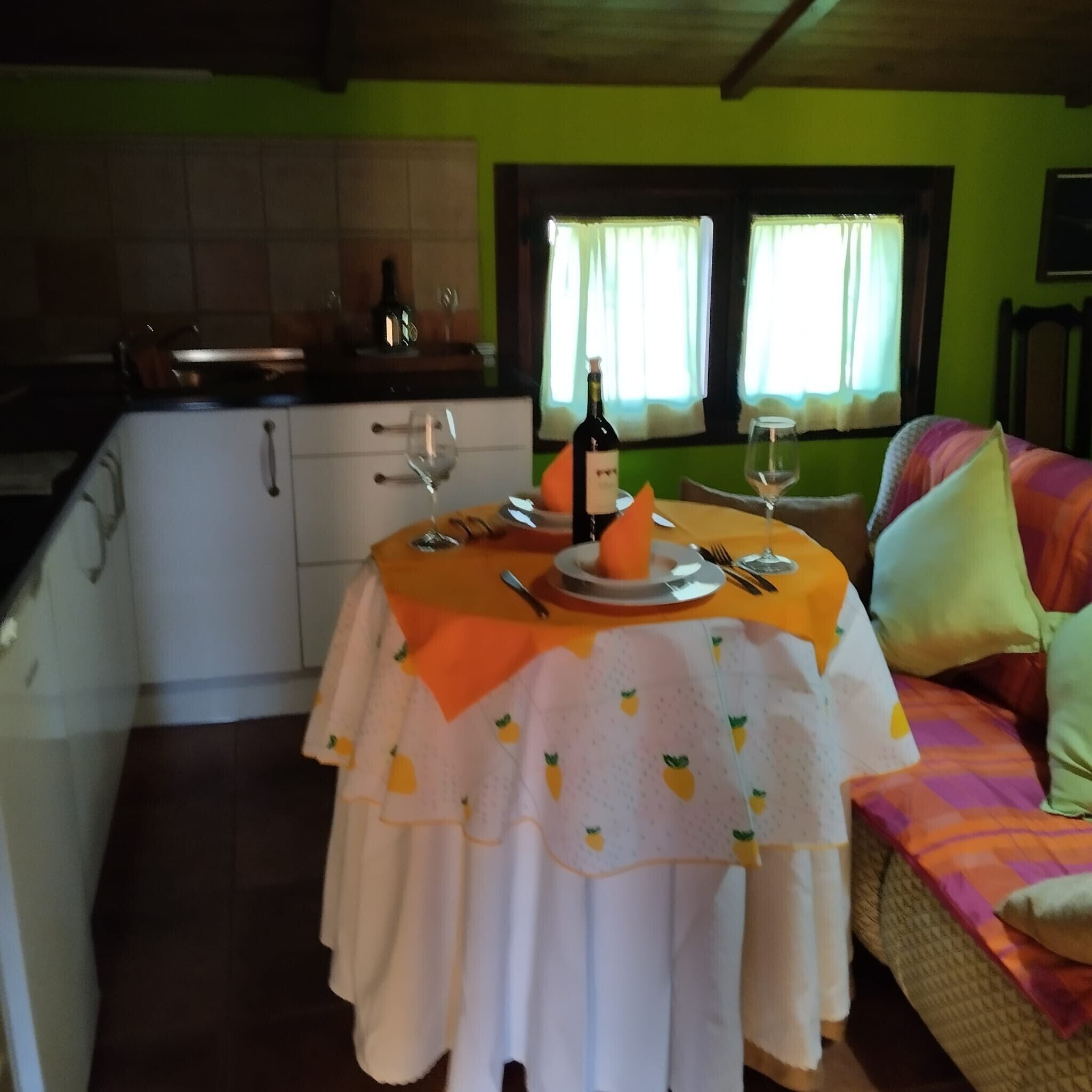 Comedor con una mesa dispuesta para dos personas, una botella de vino y una ventana con cortinas.
