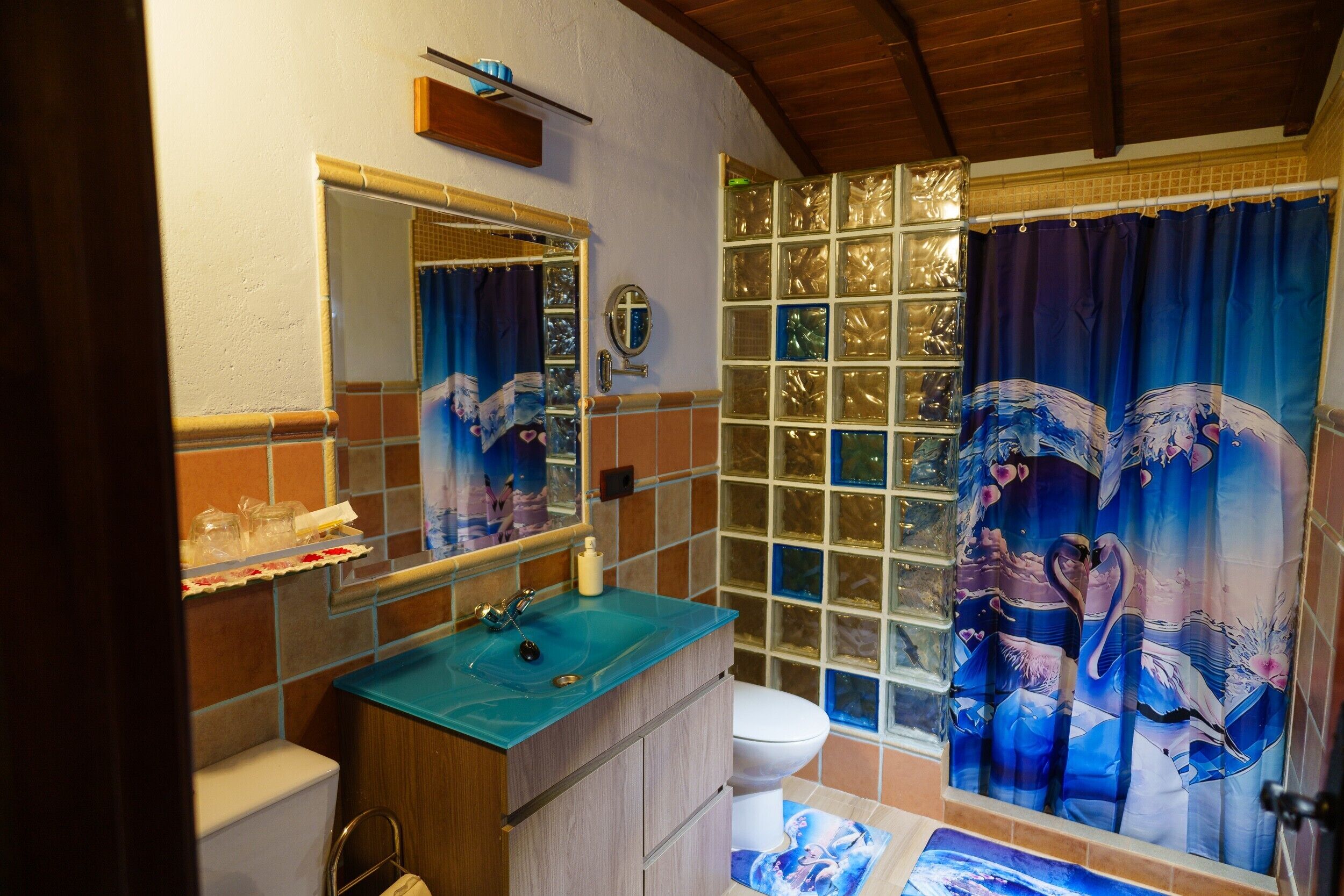 Ein Badezimmer mit blauem Waschbecken, Toilette, Spiegel und einer Duschkabine mit floralem Muster.