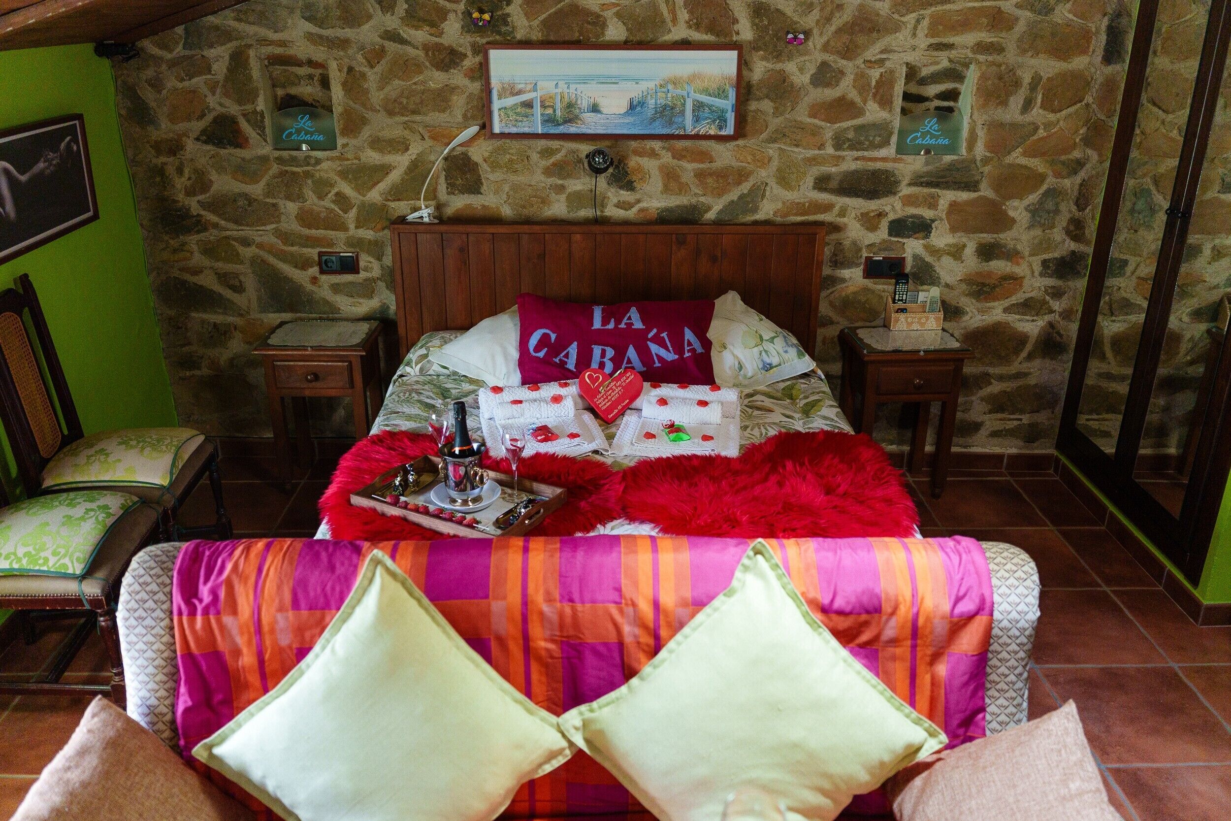 Un dormitorio con paredes de piedra, una cama, una mesita de noche, una lámpara y un cuadro en la pared.