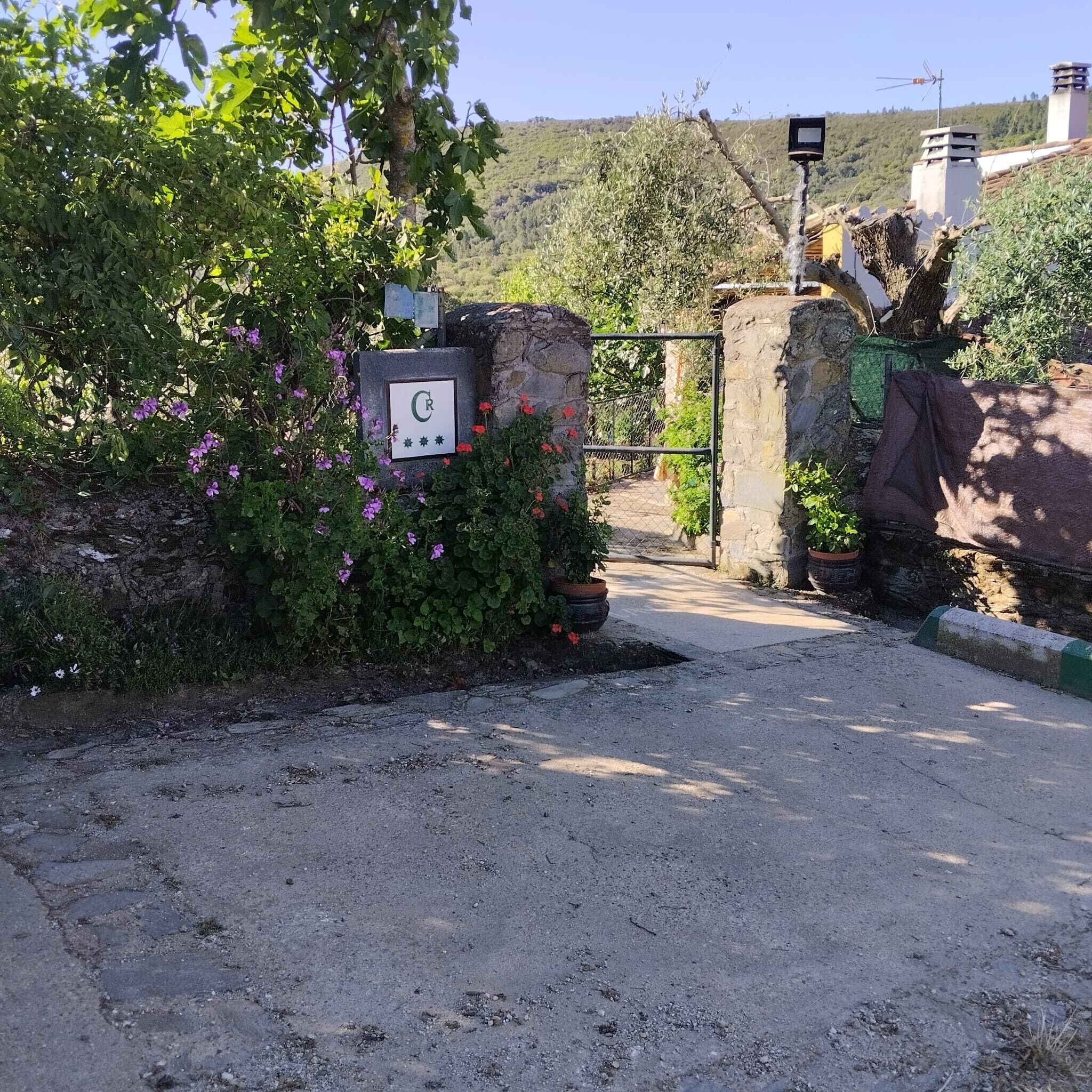 A gated entrance with a stone wall, a sign with a letter, and a view of a hilly landscape.