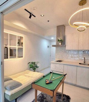 A compact living space with a pool table, a sofa, a kitchen area, and a ceiling-mounted light fixture. - R&N Azure Staycation (Parañaque)