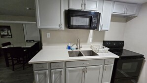 A kitchen with white cabinets, a black microwave, a sink, and a stove.