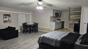 A bedroom with a bed, a dining table with chairs, a kitchenette, and a ceiling fan.