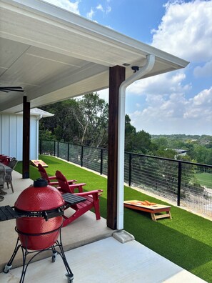 Ein überdachter Außenbereich mit Grill, roten Stühlen und Blick auf eine grüne Rasenfläche und Bäume.