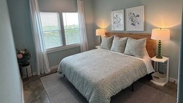 Ein Schlafzimmer mit einem Bett, zwei Nachttischlampen, einem Deckenventilator, einem Fenster mit Vorhängen und zwei gerahmten Bildern an der Wand.
