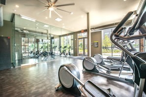 Ein Fitnessraum mit Trainingsgeräten, einem großen Spiegel und einem Deckenventilator.