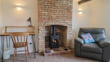 A cozy room with a brick fireplace, a leather sofa, a wooden chair, and a desk.