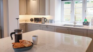 A kitchen with a marble countertop, a coffee maker, a cup, and croissants.