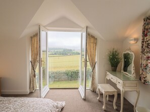 Ein Schlafzimmer mit großem Fenster, einem Bett, einem Schminktisch, einem Spiegel und einem kleinen Tisch.