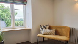 A corner room with a window, a sofa, a radiator, and a potted plant.