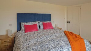 A bed with a patterned bedspread, two pillows, a blue headboard, and a wooden nightstand with a lamp.
