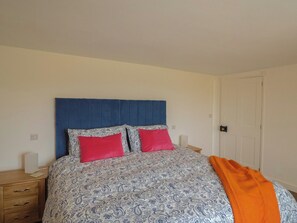 Una cama con una colcha estampada, dos almohadas, un cabecero azul y una mesita de noche de madera con una lámpara.